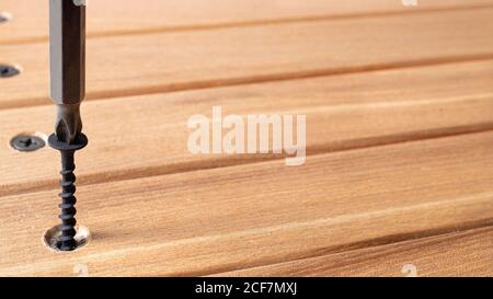 The screwdriver twists the self-cut into wooden boards. Construction tools, home repairs. Stock Photo