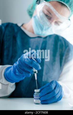 Young female medical specialist in protective mask and gloves filing syringe with vaccine from vial for prevention and immunization from coronavirus infection Stock Photo