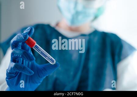 Crop anonymous medical worker in protective uniform and latex gloves holding test tube with blood sample for coronavirus test while working in lab Stock Photo