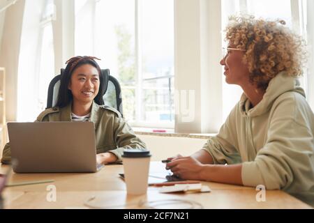 Two business colleagues sitting at the table with laptop and documents and talking to each other during the meeting Stock Photo