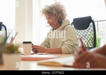 Mature businesswoman using her mobile phone while sitting at the table during meeting at office Stock Photo