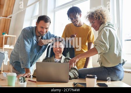 Group of designers sitting at the table and looking at monitor of laptop they developing new project together Stock Photo