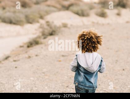 Back view of anonymous curly ethnic child dressed in casual clothes on beige blurred background Stock Photo