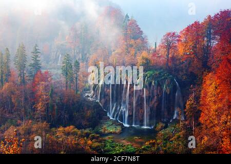 Incredible view on foggy waterfall in Plitvice lakes. Orange autumn forest on background. Plitvice National Park, Croatia. Landscape photography Stock Photo