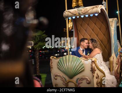 Happily married young man in blue suit and Woman in wedding dress looking at each other while taking amusement rides in an embrace with Eiffel Tower on background Stock Photo