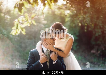 Smiling groom and bride hugging and kissing in park Stock Photo