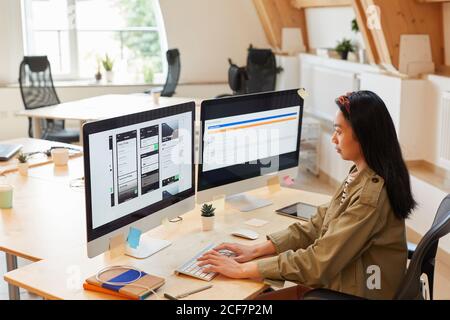 Asian young woman sitting at the table typing on computer keyboard she testing new software at office Stock Photo