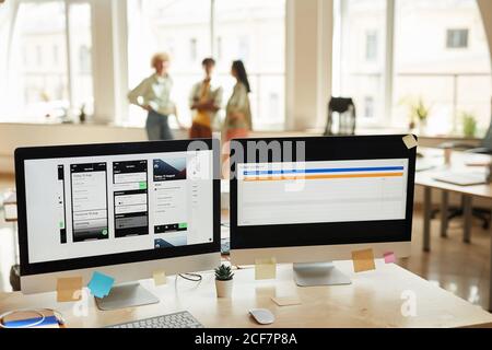 Image of computer monitors with new software on the table at office with people working in the background Stock Photo