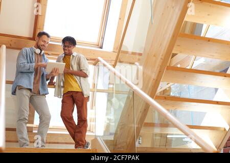 Two men standing on stairs watching something on digital tablet and discussing it Stock Photo