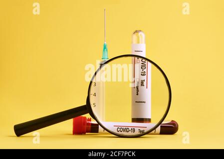 Closeup of coronavirus blood test sample and medical syringe seen through magnifying glass on yellow background Stock Photo