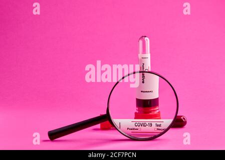 Closeup of coronavirus blood test sample seen through magnifying glass on pink background Stock Photo