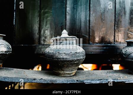 Old gray stone jug with lid located on wooden shelf against wall in market Stock Photo