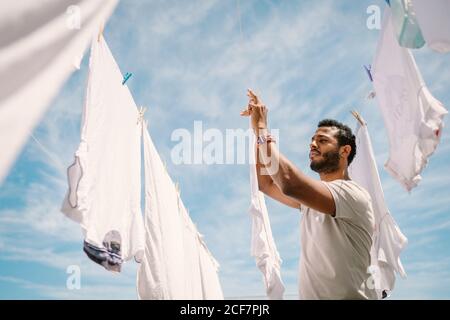 Diligent ethnic man hanging t-shirt on rope Stock Photo