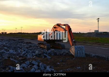 Excavator at construction site on sunset background. Earth-moving heavy equipment for digg ground, foundation and trenchs for laying sewer pipes and w Stock Photo