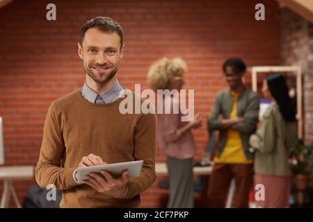Portrait of business leader smiling at camera while using digital tablet with his team standing in the background Stock Photo