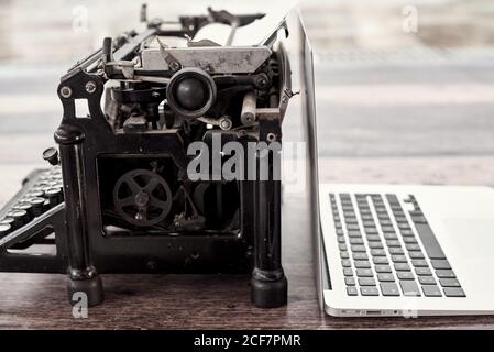 Modern netbook and old fashioned typewriter placed on wooden table on terrace Stock Photo