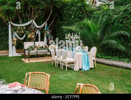 Decoration for open air wedding ceremony with dinner table in blue and white colors and wedding arch setting on garden with green tropical plants Stock Photo