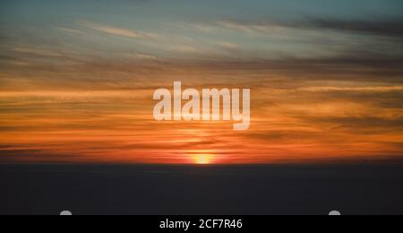 From above blurred gray horizon with hiding sun under beautiful colorful clouds on sky with wonderful transition at dusk Stock Photo