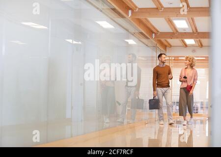 Two business colleagues talking to each other while walking along the modern office corridor Stock Photo