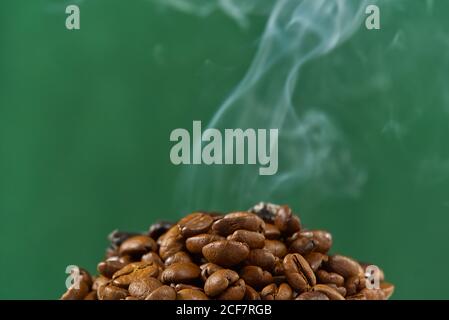 International day of coffee concept. close-up pile of coffee beans on green background with smoke on top. Stock Photo