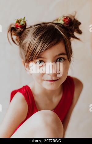 Adorable girl with fresh strawberries in hair buns smiling and looking at camera Stock Photo