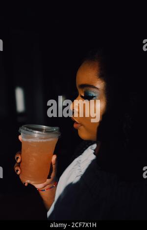 Side view portrait of backlit beautiful curvy black young Woman with bright make-up in off-shoulder dress having a cold beverage drink Stock Photo