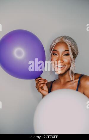 Joyful Black adult female with colorful balloons looking at camera while standing on white background Stock Photo