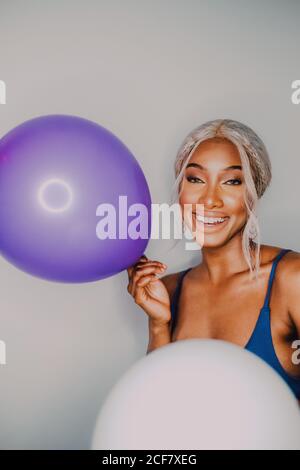 Joyful Black adult female with colorful balloons looking at camera while standing on white background Stock Photo