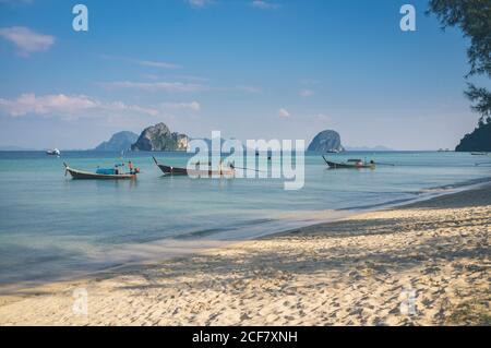 Small boats floating on calm sea water near sandy shore on sunny day in Thailand