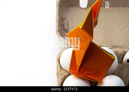 Origami rabbit from orange colored paper. Easter bunny and white chicken eggs in the box, copy space Stock Photo