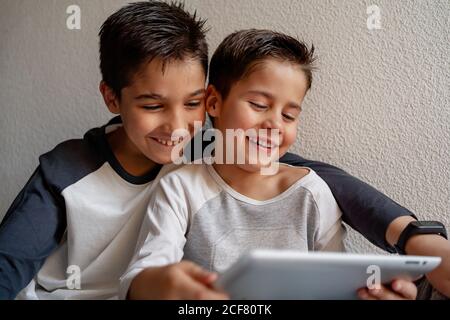 Smiling brothers in sleepwear sitting on cozy bed and watching movie together while entertaining at home Stock Photo