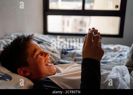 Delighted boy using tablet in bedroom during weekend Stock Photo