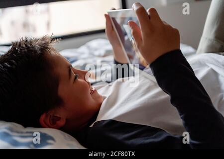 Delighted boy using tablet in bedroom during weekend Stock Photo