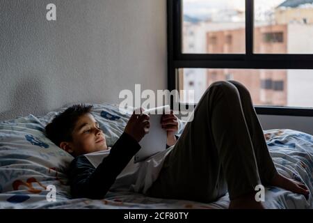 Delighted boy using tablet in bedroom during weekend Stock Photo