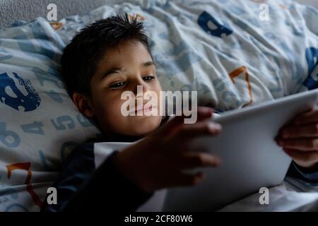 Delighted boy using tablet in bedroom during weekend Stock Photo