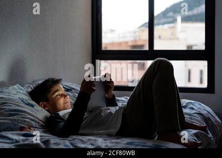 Delighted boy using tablet in bedroom during weekend Stock Photo