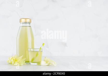 Fresh vegetable green celery juice in glass bottle mock up with glass, straw, stems in soft light white interior on wood table. Stock Photo