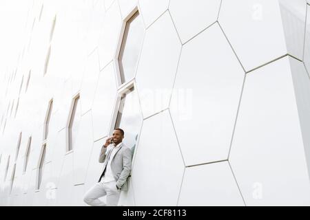 Elegant black man talking smartphone leaning on geometrical wall Stock Photo