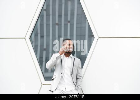 Elegant black man talking smartphone leaning on geometrical wall Stock Photo
