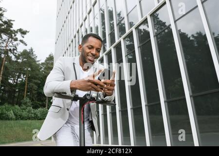 Smiling black man riding scooter and speaking on smartphone Stock Photo
