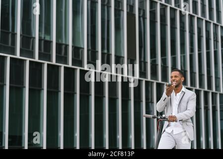 Smiling black man riding scooter and speaking on smartphone Stock Photo