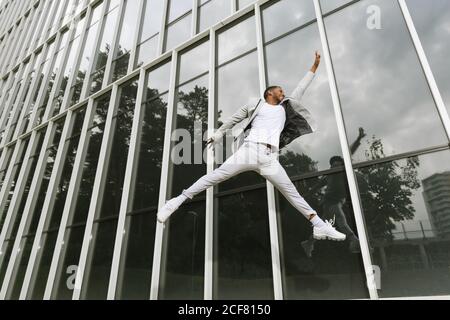 Side view of handsome African American businessman celebrating victory raising hand and jumping high on background of glass wall Stock Photo