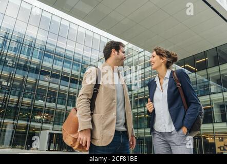 Delighted colleagues smiling and looking at each other while walking outside contemporary building after work Stock Photo