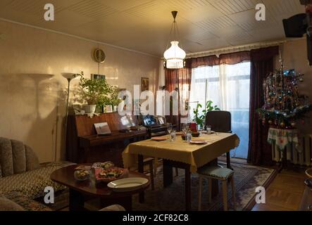 Interior of typical simple cozy living room decorated for Christmas dinner with arranged table and retro styled Christmas tree Stock Photo