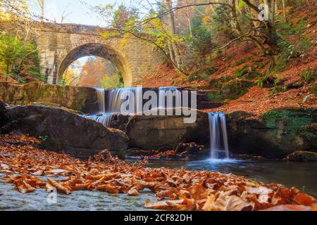 Autumn waterfall under stone bridge in the mountain Stock Photo