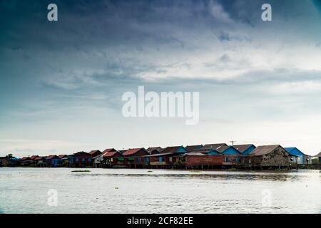 View of small remote village with poor houses above water under cloudy sky, Cambodia Stock Photo