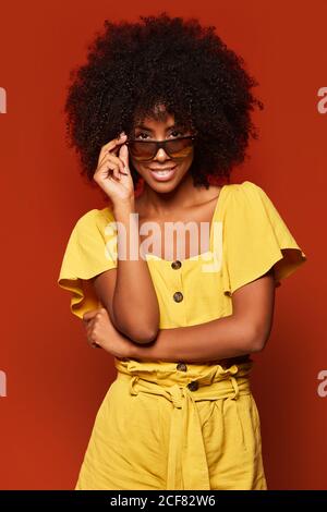 Modern young black Woman with Afro hairstyle posing while smiling at camera on bright red background Stock Photo