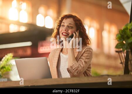 Young Woman talking on phone while working on laptop Stock Photo