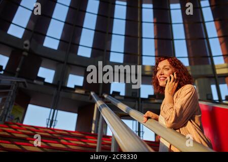 Charming red haired young Woman talking on phone in airport while waiting for train to departure Stock Photo