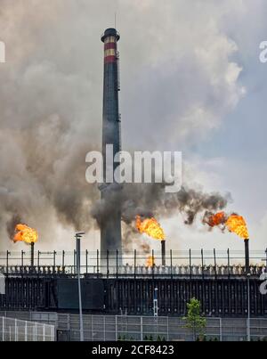 Weathered industrial buildings and pipes emitting smoke and flames at coking factory Stock Photo